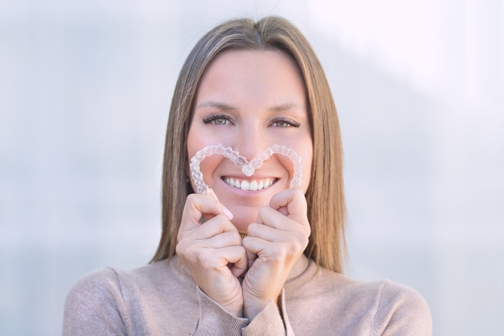 Woman with bright smile holding her upper and lower Invisaligners.