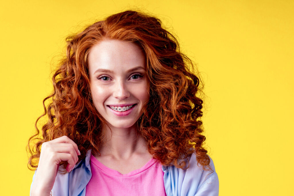 A redheaded woman smiling brightly at the camera with photoshopped-on braces.