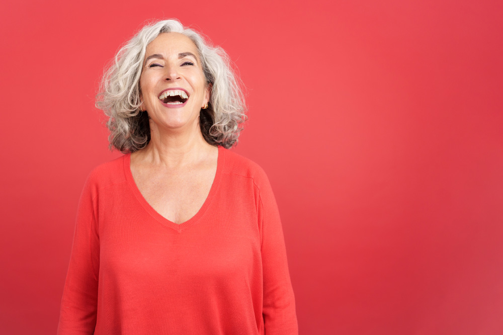 an older woman smiling wearing a red shirt in front of a red background.