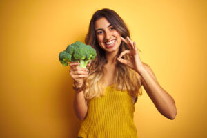 a woman wearing yellow holding broccoli.