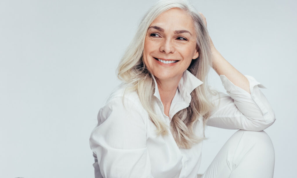 Beautiful senior woman in white casuals looking away and smiling. Cheerful mature woman sitting on white background.