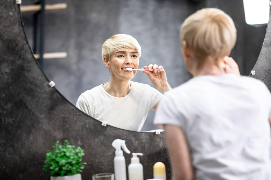 Mature Lady Brushing And Cleaning Teeth In Bathroom At Home.