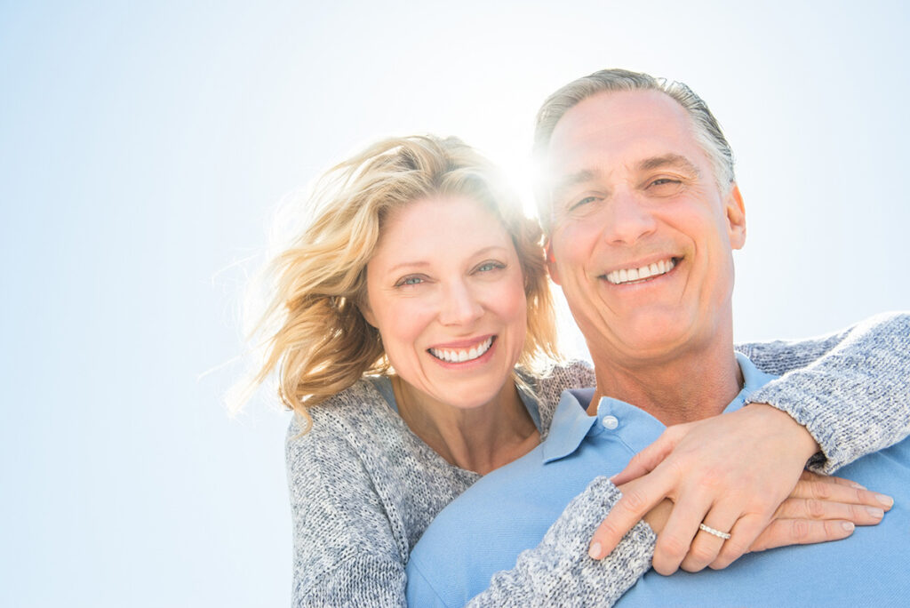 Older couple hugging and smiling together outside on a sunny day.