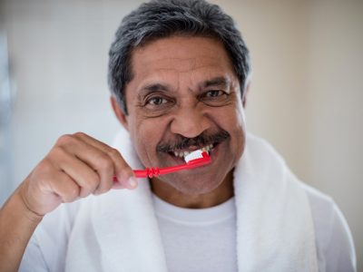 A senior man brushing his teeth in a bathroom mirror.