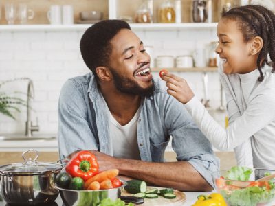 A father being fed a tomato by his playful daughter.