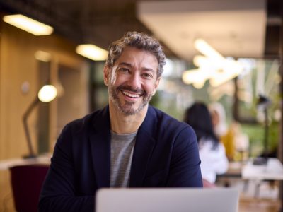 Portrait Of Mature Businessman Working On Laptop At Desk In Office