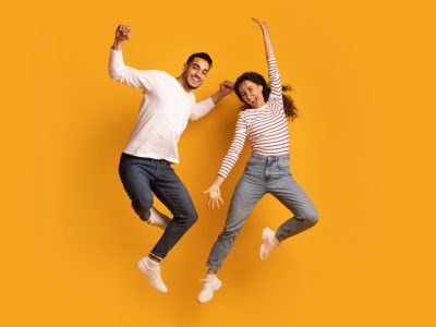 Cheerful Active Arab Couple Jumping In Air Over Yellow Background, Joyful Emotional Middle Eastern Man And Woman Having Fun Together, Raising Hands And Exclaiming With Excitement, Full Length