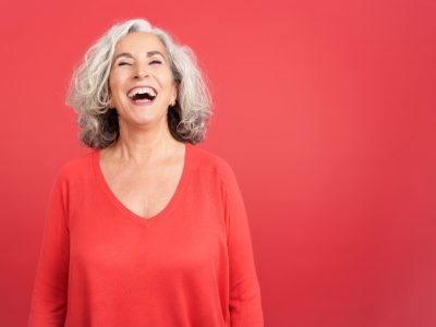 an older woman smiling wearing a red shirt in front of a red background.
