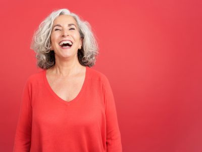 an older woman smiling wearing a red shirt in front of a red background.