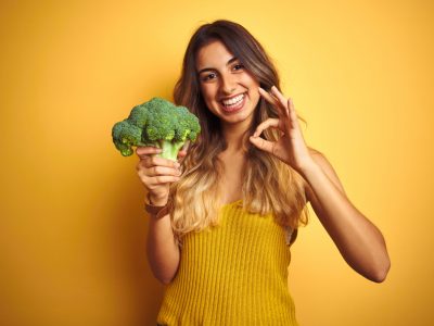 a woman wearing yellow holding broccoli.