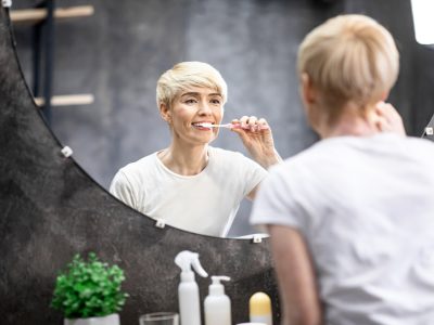 Mature Lady Brushing And Cleaning Teeth In Bathroom At Home.