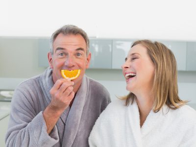 Portrait of a cheerful couple using an orange slice in place of a smile while in the kitchen.