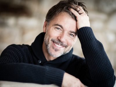A man leaning over the back of a chair smiling at the camera.