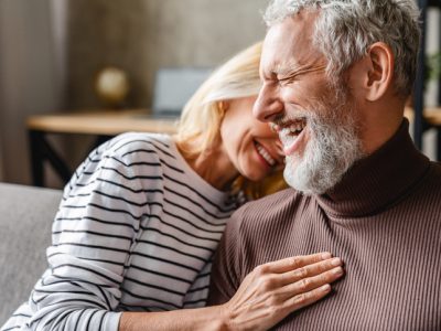 A happy, older couple laughing together on a couch.