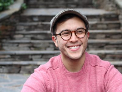 Hip man smiling wearing eyeglasses and hat.