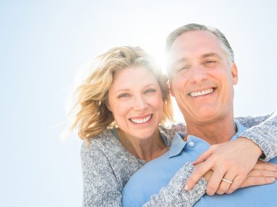 Older couple hugging and smiling together outside on a sunny day.