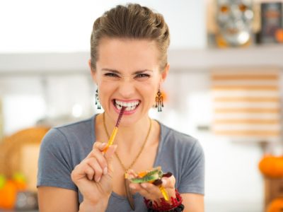 A young woman eating a gummy worm by dramatically tugging it apart.