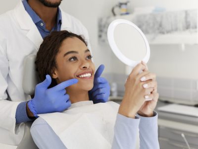A woman looking at her reflection as a dentist shows her her own teeth.