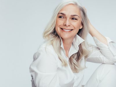 Beautiful senior woman in white casuals looking away and smiling. Cheerful mature woman sitting on white background.
