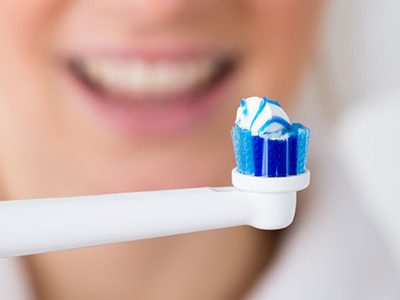 close-up of toothbrush with toothpaste in front of woman - Dental News.